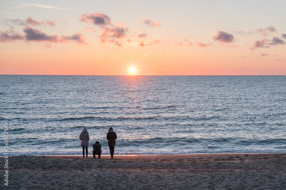 Very beautiful sunset on the Baltic Sea. People walk by the sea. The sea is calm.