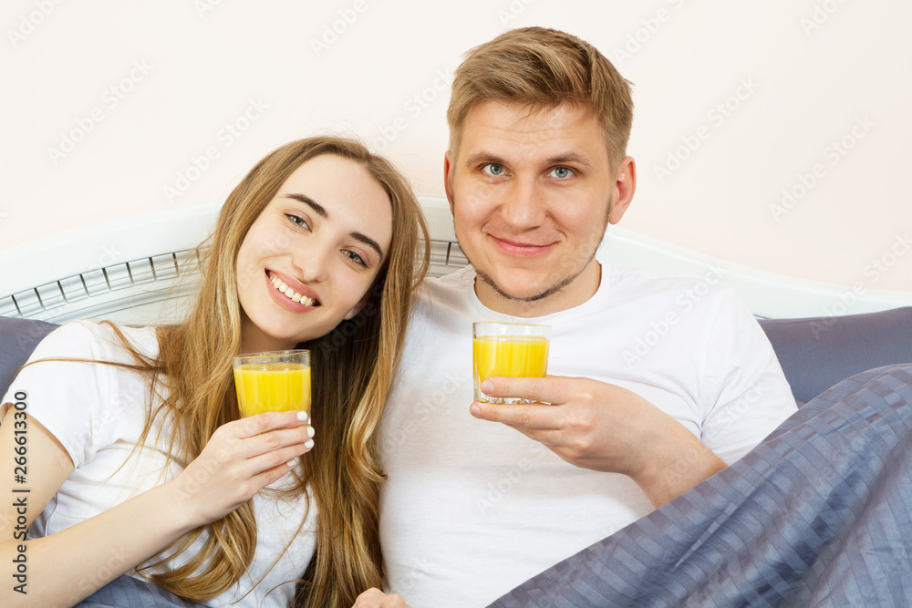 Happy relaxed young couple with orange juice in bed at home. Romantic couple drinking orange juice lying on their bed. Happy relaxed young couple with orange juice in bed at home. Romantic couple drinking orange juice lying on their bed.