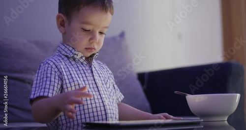 Cute Child Entertaining With Tablet. Little Boy Spending Leisure Time Playing Mobile Game in the and Crushes the Bright Screen With Her Hand. Concept of:Happy Childfood, Technology, Childen Play Games photo