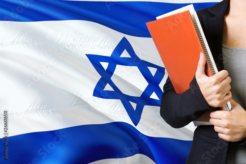 Learning Israeli language concept. Young woman standing with the Israel flag in the background. Teacher holding books, orange blank book cover. photo