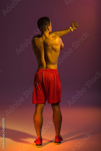 back view of athleltic man in red shorts warming up on purple background photo