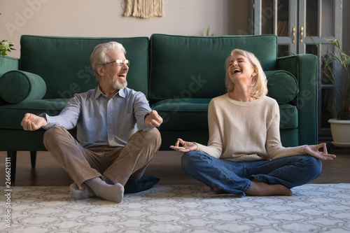 Happy mature couple having fun, practicing yoga together at home