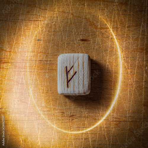 Fehu. Handmade scandinavian wooden runes on a wooden vintage background in a circle of light. Concept of fortune telling and prediction of the future.