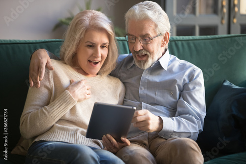 Surprised mature wife and husband using tablet, reading pleasant news