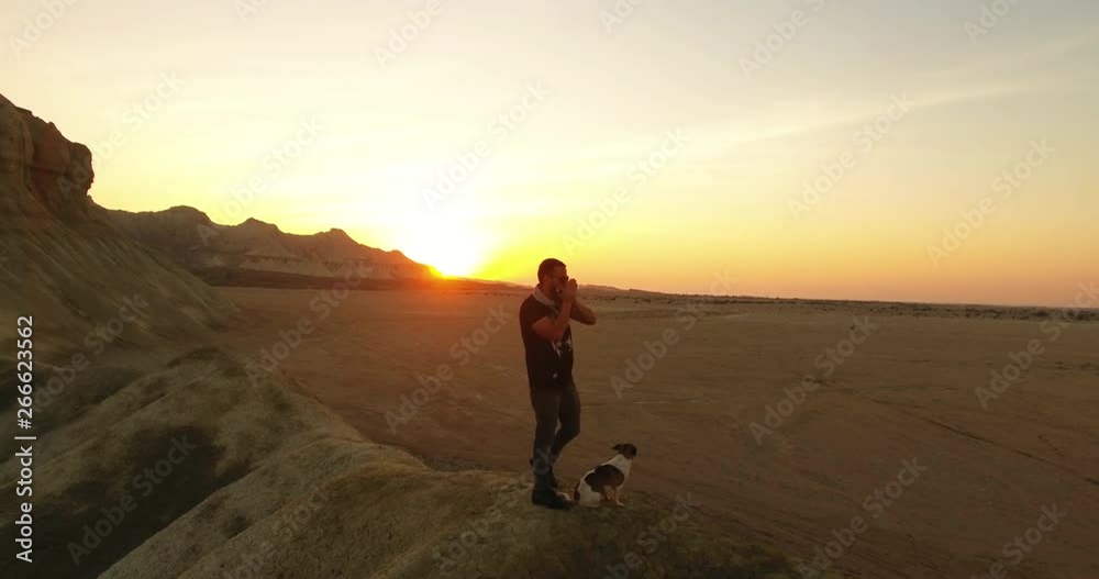 A rotating aerial shot of a man and his dog playing harmonica during sunset 3 An aerial shot of a man and his puppy standing on top of a hill and playing harmonica long shadows golden hour A rotating aerial shot of a man and his dog playing harmonica during sunset 3 An aerial shot of a man and his puppy standing on top of a hill and playing harmonica long shadows golden hour