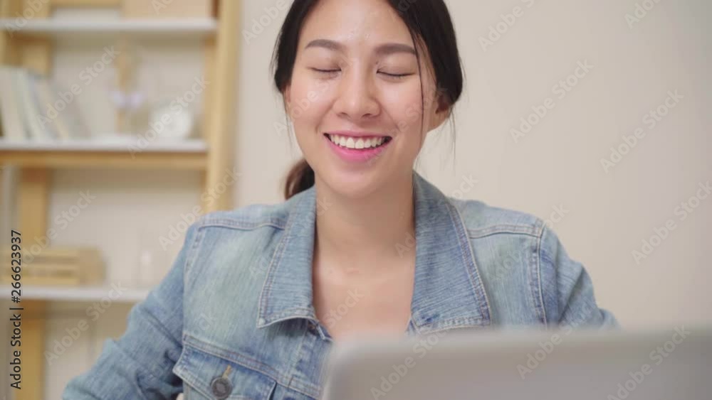Asia business woman feeling happy smiling and looking to camera while relax at home office. Young asian woman working using laptop on desk in living room at home. Asia business woman feeling happy smiling and looking to camera while relax at home office. Young asian woman working using laptop on desk in living room at home.