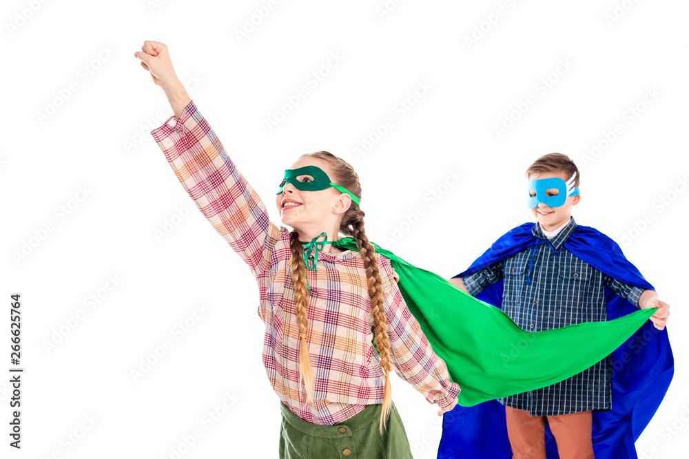 boy holding cape of smiling kid in superhero costume posing with outstretched hand isolated On White