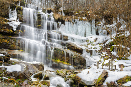 Hanging ice formations and semi-frozen waterfall Tupavica during winter on Old mountain in Serbia  near Pirot. Cold winter colors are contrasted by hot colors of rocks and grass.