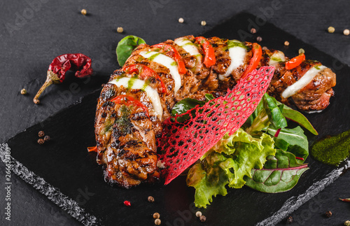 Baked Veal with mozzarella cheese, tomatoes, pesto sauce and green salad on black sbackground. Hot Meat Dishes photo