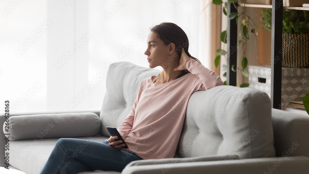 Serious woman sitting on couch in living room with phone Serious woman sitting on couch in living room with phone
