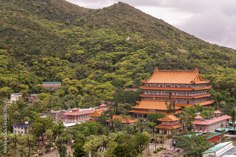 Hong Kong, China - March 7, 2019: Lantau Island. Po Lin Buddhist Monastery seen from platform at Tian Tan Buddha statue. Red roofs between trees and green hill in back.