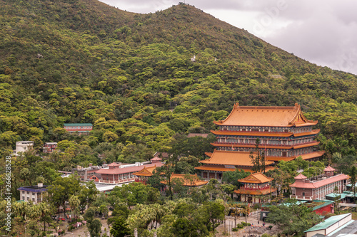 Hong Kong, China - March 7, 2019: Lantau Island. Po Lin Buddhist Monastery seen from platform at Tian Tan Buddha statue. Red roofs between trees and green hill in back.