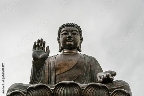 Hong Kong, China - March 7, 2019: Lantau Island. Frontal Facial closeup of Tian Tan Buddha statue from down under showing face, chest, and lotus leaves under silver sky.