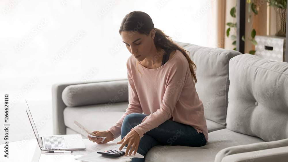 Focused woman calculating bills sitting on couch at home Focused woman calculating bills sitting on couch at home