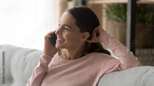 Closeup smiling woman sit on couch talking on mobile phone