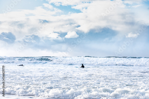 Surfing sport scenery. Two male surfers sporting in waters of Norwegian sea on Unstad beach on Lofoten islands in Norway. Arctic surfing. Extreme sport in northern sea. Epic northern seascape.