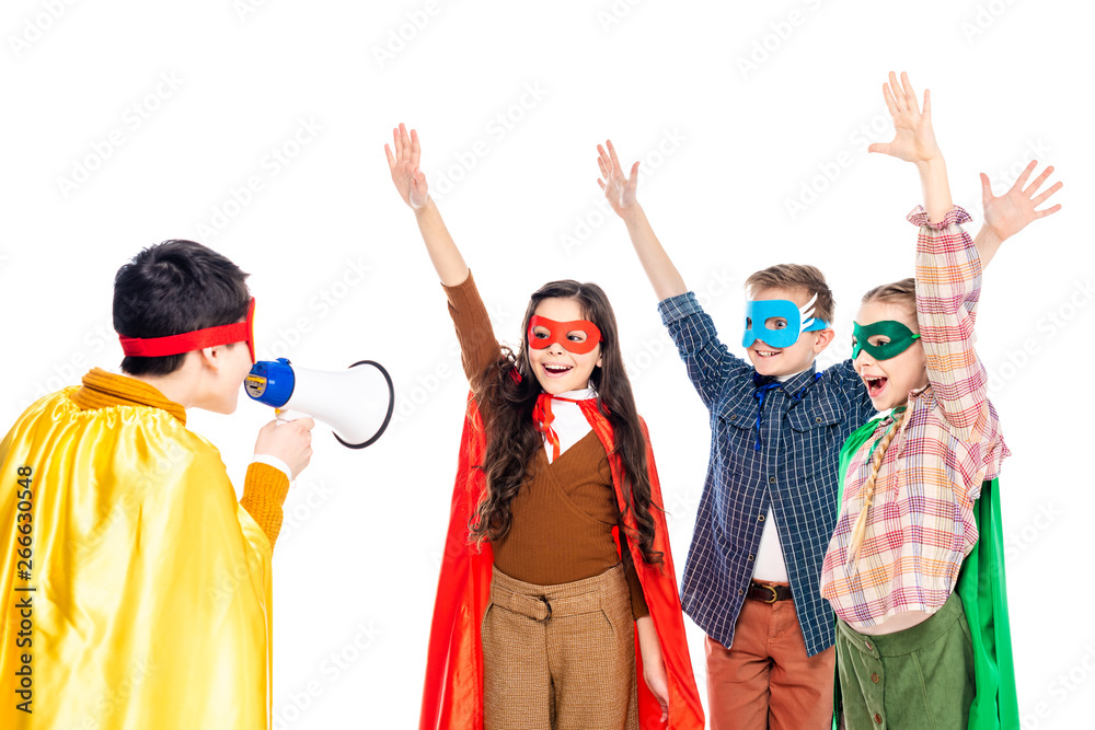 happy kids in superhero costumes raising hands while boy shouting in mouthpiece Isolated On White