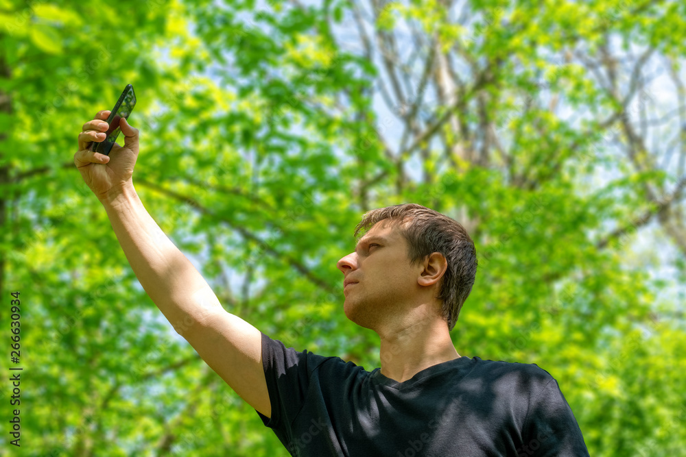 Man with his mobile smart phone searching for reception signal in the forest.