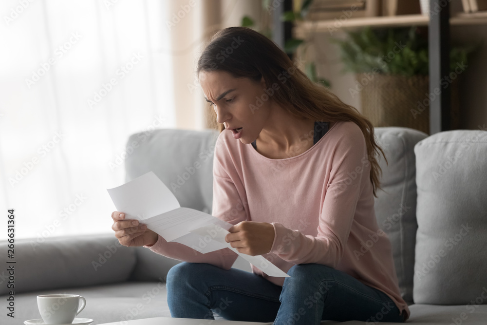 Angry woman sitting on couch holding letter received bad news - obrazy, fototapety, plakaty 