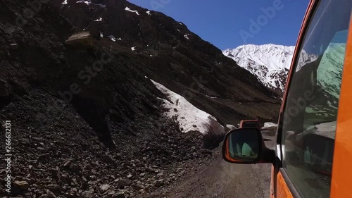 Looking forward from out the back seat windowof an orange van at the tall, snow capped mountains ahead photo