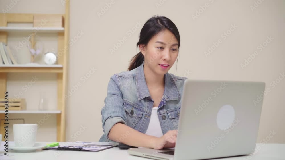 Asia business woman feeling happy smiling and looking to camera while relax at home office. Young asian woman working using laptop on desk in living room at home. Asia business woman feeling happy smiling and looking to camera while relax at home office. Young asian woman working using laptop on desk in living room at home.