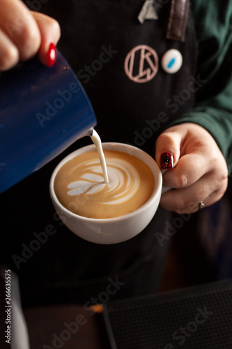 Female barista making rosetta latte art on cappuccino milk foam