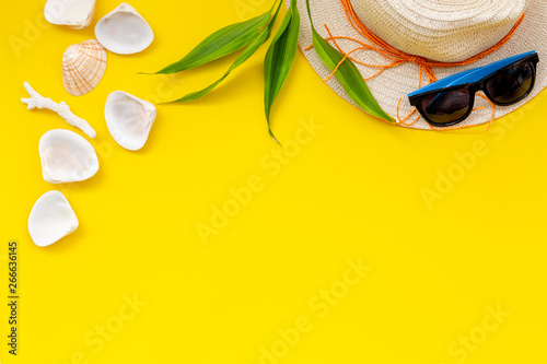 Planning vacation to the seaside with straw hat, sun glasses, shells on yellow background top view space for text