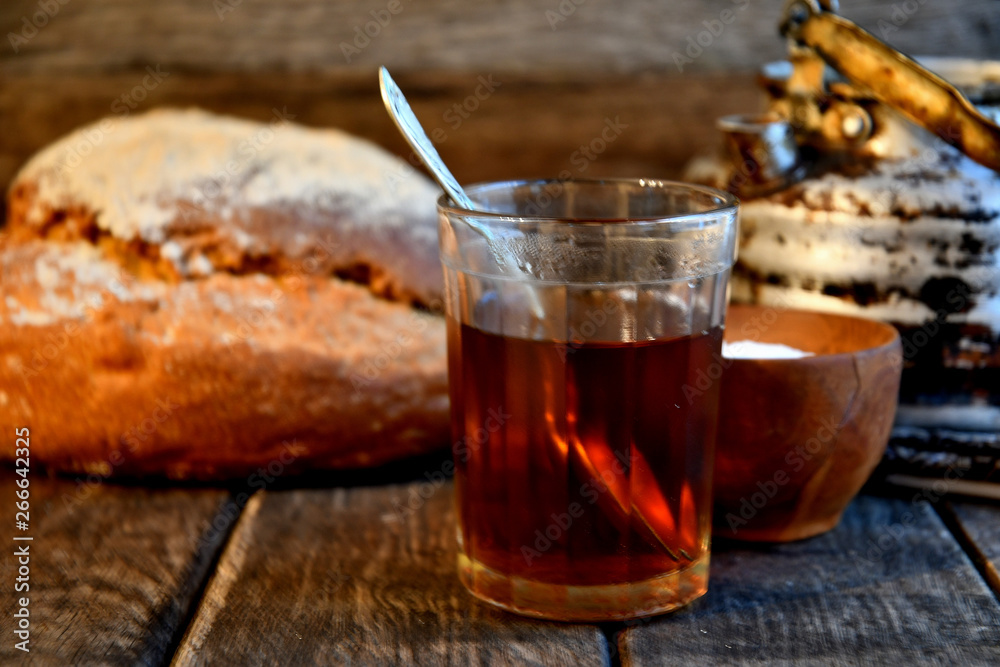 Bread, sugar, black tea in a glass, an old aluminum kettle on a wooden background. Bread, sugar, black tea in a glass, an old aluminum kettle on a wooden background.