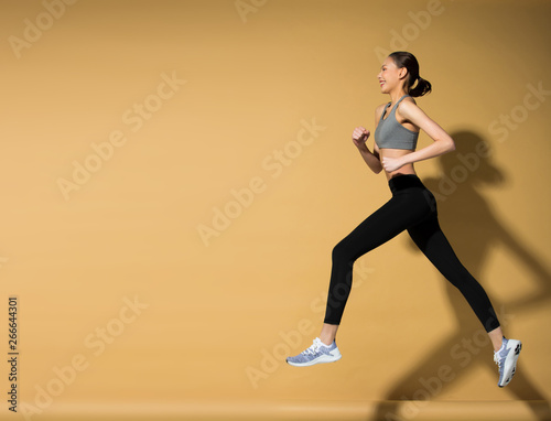 Asian slim Fitness woman exercise warm up stretch spring jumps legs, studio lighting yellow beige mustard background sun shadow copy space, concept Woman Can Do athlete Sport 6 packs