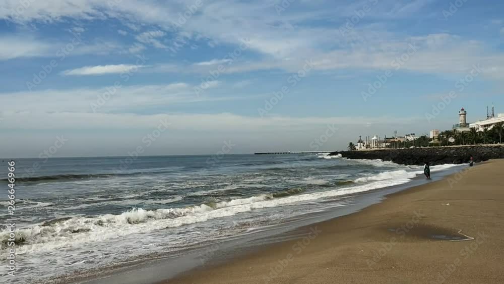 Bright serene morning beach view with spread clouds with blue sky. The sea water is so vibrant with active waves on the shore with city buildings on one backgorund. Bright serene morning beach view with spread clouds with blue sky. The sea water is so vibrant with active waves on the shore with city buildings on one backgorund.