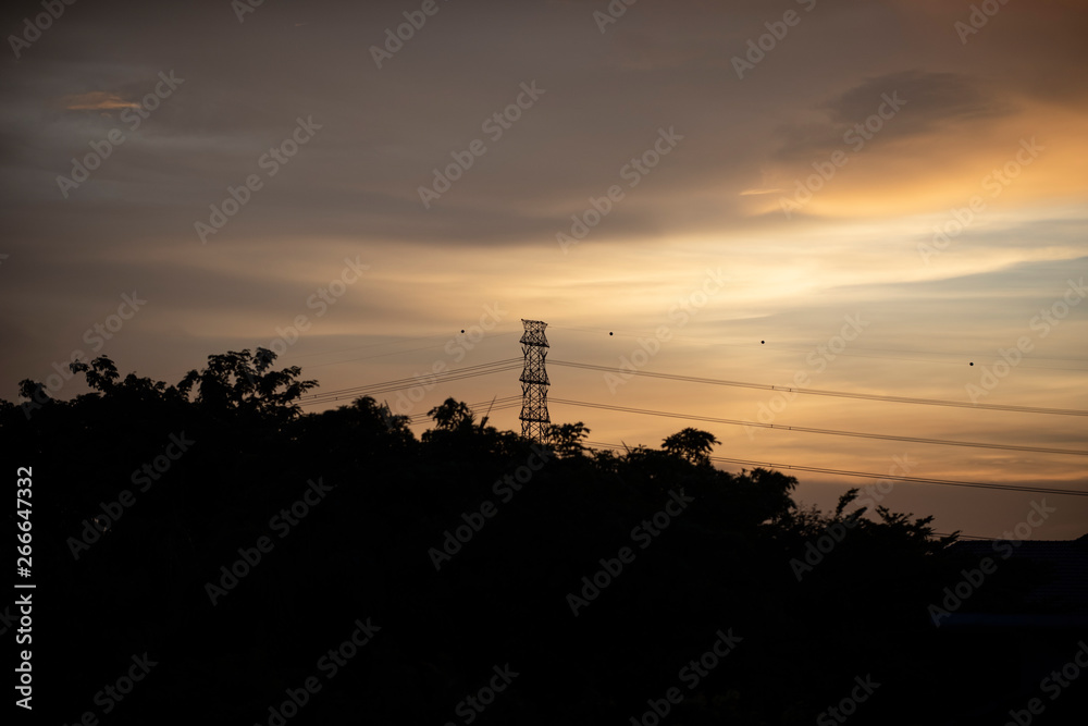 High voltage electricity pillars and power pylons in a silhouette image against a beautiful sunset as a background.