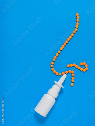 The figure of a nose of orange tablets and nasal spray on a blue background. The concept of treatment of diseases of the nose and allergies. Flat lay.