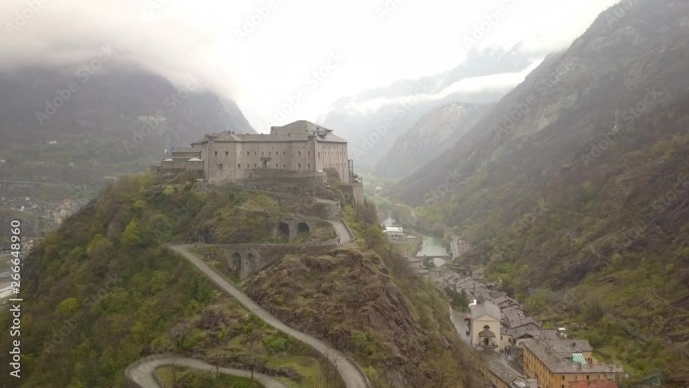 Magnificent rainy aerial view Aosta Valley, northwestern Italy. Drone flies forward overlooking historical medieval castle Forte di Bard. Moody overcast Italian alp landscape scenery. Magnificent rainy aerial view Aosta Valley, northwestern Italy. Drone flies forward overlooking historical medieval castle Forte di Bard. Moody overcast Italian alp landscape scenery.