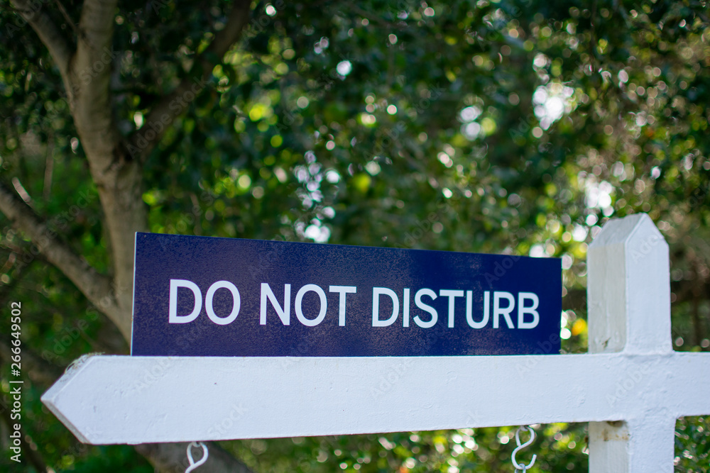 Do not disturb warning sign in rural area with blurred green trees in background