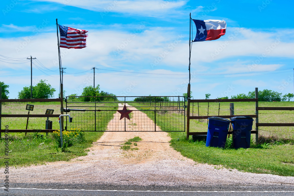 American and Texas state flags flying near countryside gate, Texas rustic star with road to the house slowly dissolving in the background. American and Texas state flags flying near countryside gate, Texas rustic star with road to the house slowly dissolving in the background.