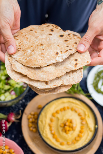 Woman hands holds hot homemade baked whole wheat flour Indian chapati crispy flat breads, pita, roti or paratha. Vegan food, vegetarian healthy food.