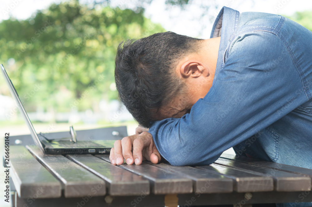 Fototapeta premium A man taking a break by sitting with falling his head down on the desk after using laptop in a public park