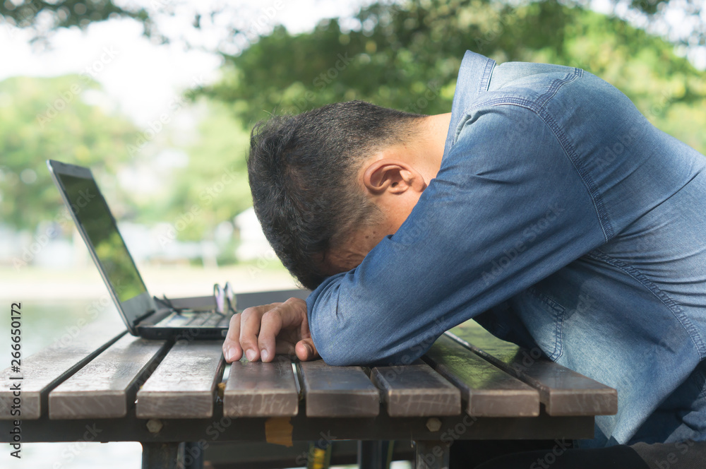 A man taking a break by sitting with falling his head down on the desk after using laptop in a public park A man taking a break by sitting with falling his head down on the desk after using laptop in a public park