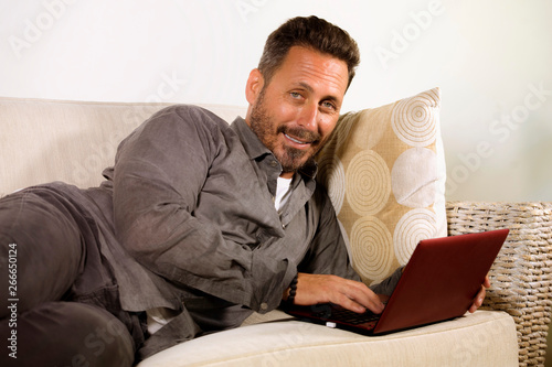 natural lifestyle portrait of young handsome and successful self employed man working at home using laptop computer lying relaxed at living couch networking