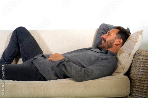 lifestyle home portrait of young attractive and happy white man with beard and casual shirt lying relaxed and cozy at living room sofa couch resting and smiling cheerful © TheVisualsYouNeed