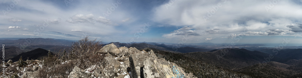Panoramic view from the top of the mountain: mountains covered with forests, hills, rocks and blue sky with white clouds. Panoramic landscape image Panoramic view from the top of the mountain: mountains covered with forests, hills, rocks and blue sky with white clouds. Panoramic landscape image