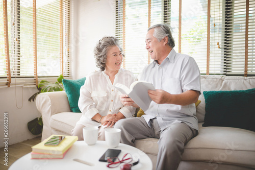 Happy senior couple sitting at sofa in living room and reading a book together. Take a moment of happiness together.