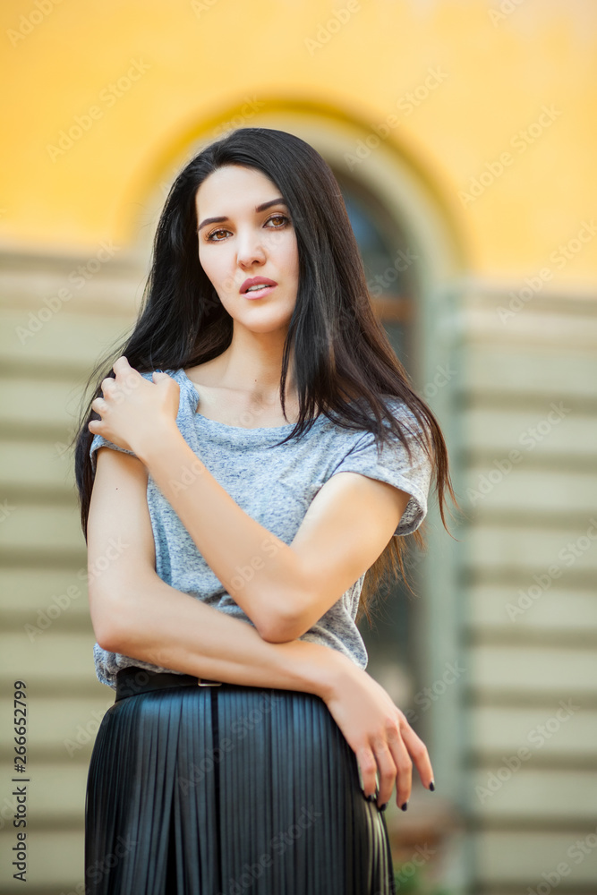 cute young girl posing near building. sweet woman in a gray shirt and a black leather skirt walking around city. Concept of modern freedom hipster human cute young girl posing near building. sweet woman in a gray shirt and a black leather skirt walking around city. Concept of modern freedom hipster human