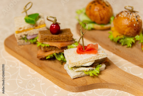 Close-up of small sandwiches and hamburgers on chopping boards in restaurant interiors.