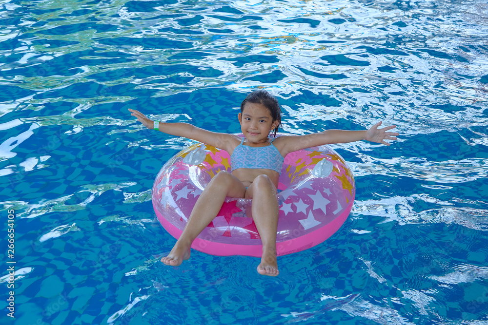 Asian Girl (9-10) sitting on pink inflatable ring in swimming pool, summer vacation concept