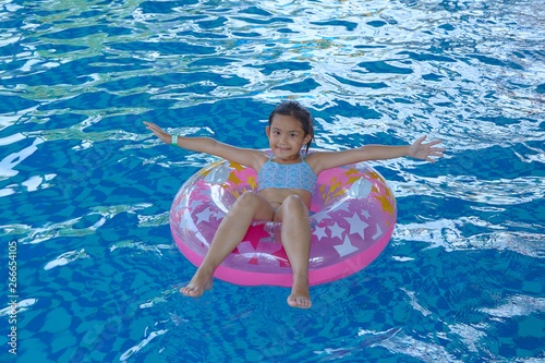 Asian Girl  9-10  sitting on pink inflatable ring in swimming pool  summer vacation concept