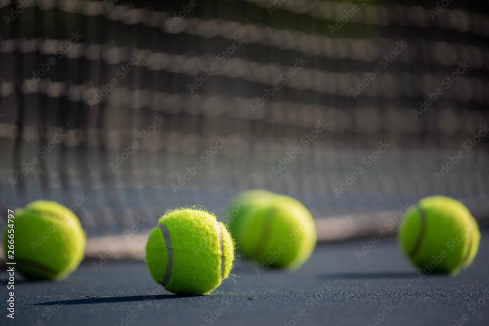 A group of yellow tennis ball on a court with net in background. Sports or exercise background.