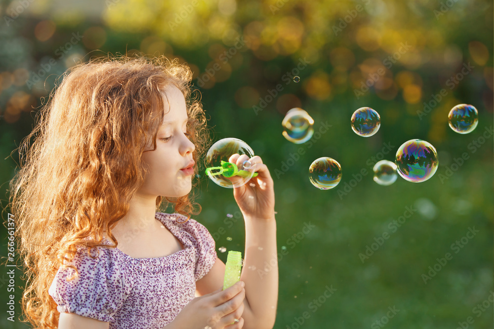 Little girl blowing soap bubbles in spring outdoors.