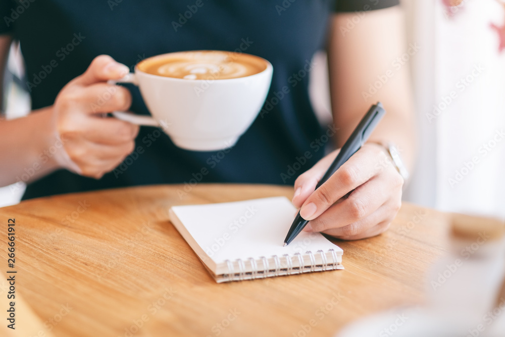 Closeup image of a woman writing on blank notebook while drinking coffee Closeup image of a woman writing on blank notebook while drinking coffee
