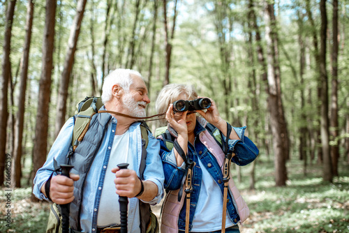 Beautiful senior couple hiking with backpacks and trekking sticks in the forest. Concept of active lifestyle on retirement